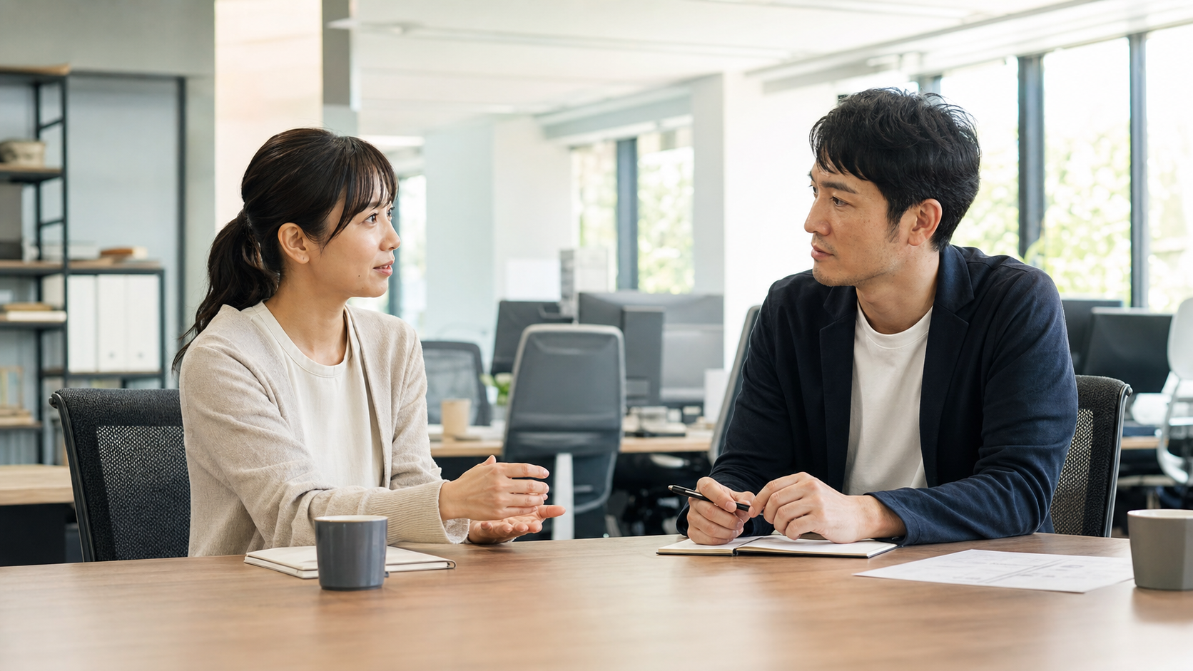 企業の採用担当者とディレクターがオフィスで打ち合わせをしている場面、明るい室内光、落ち着いたビジネス感