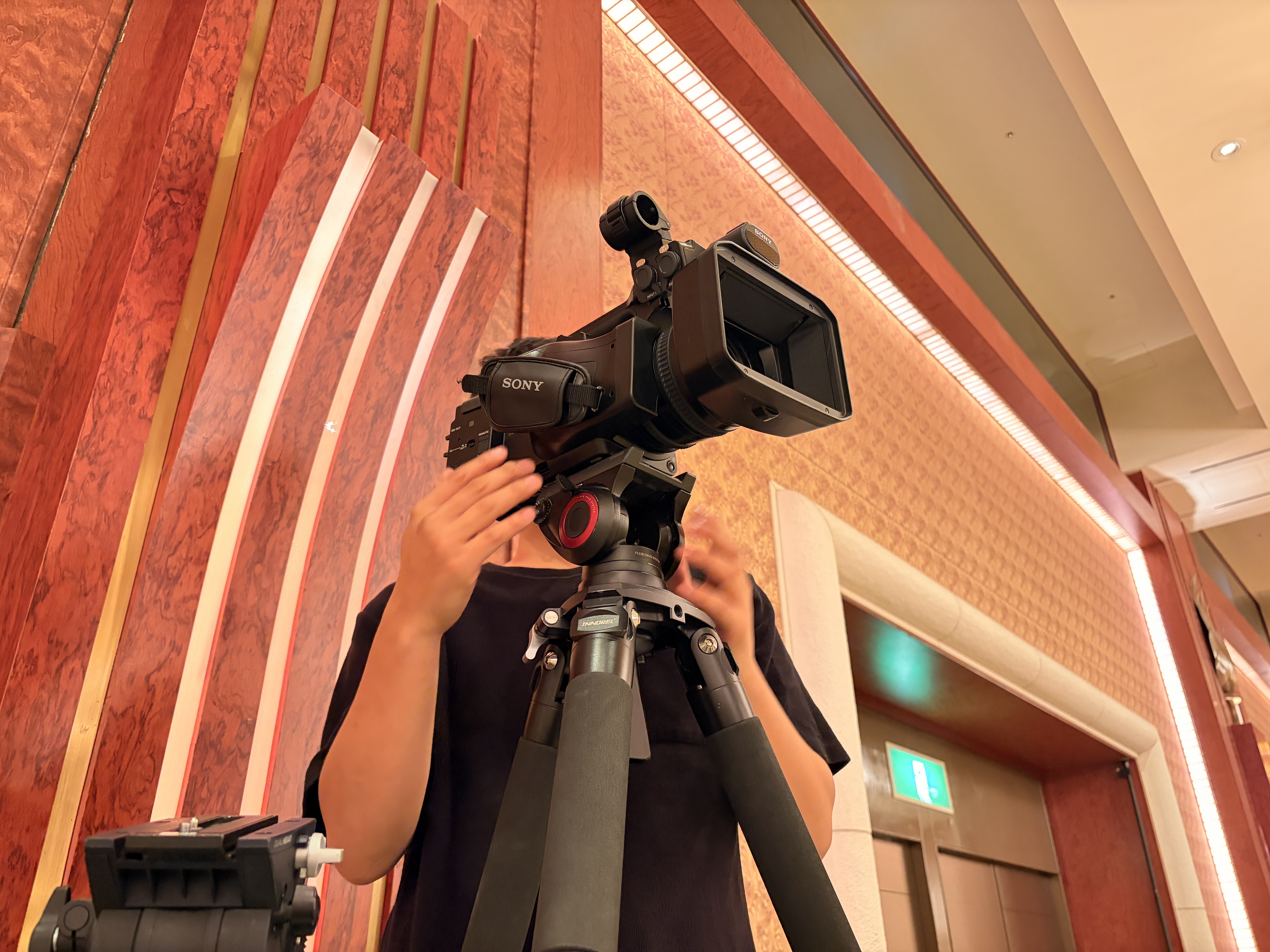 採用動画のインタビュー撮影中、社員が緊張した表情でカメラの前に座っている場面。オフィスの自然光、ドキュメンタリー風