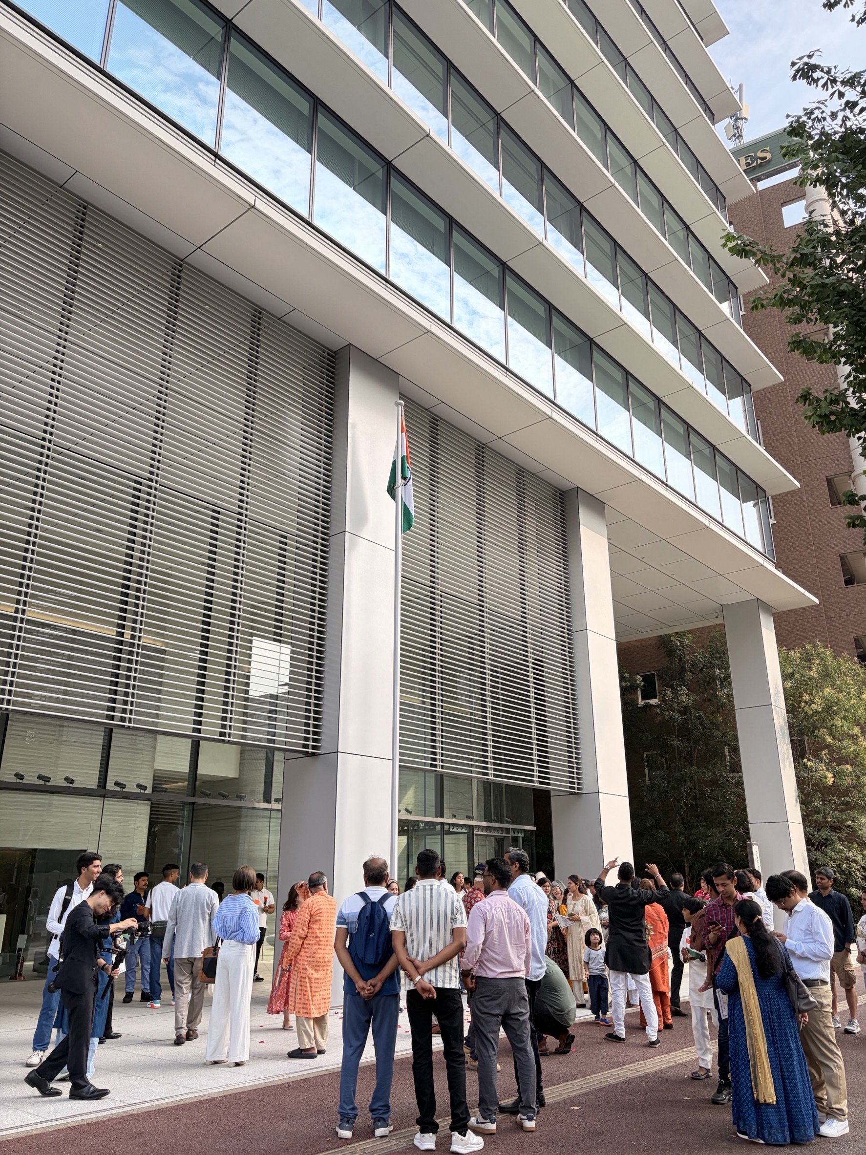 近代的なビル前にインド国旗が掲げられ、多数の人々が集まっている屋外の集会風景
