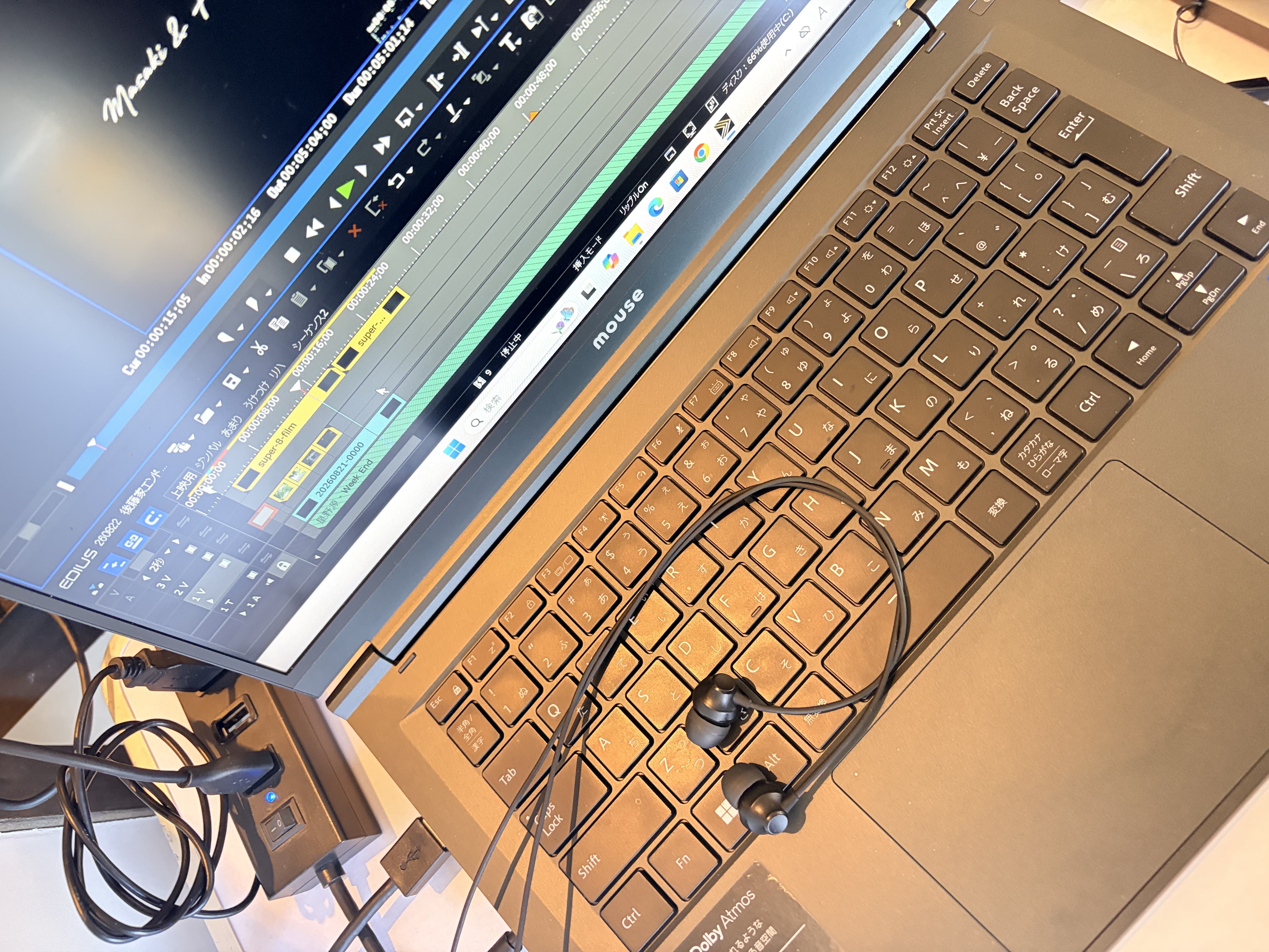 ノートPCの画面に動画編集ソフトのタイムラインが表示され、キーボード上にイヤホンが置かれている編集作業中の様子